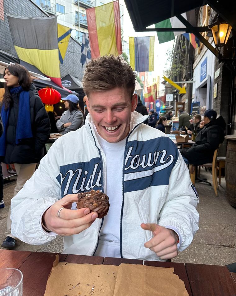 Paddy laughing while eating a cookie at an outdoor table on a busy street