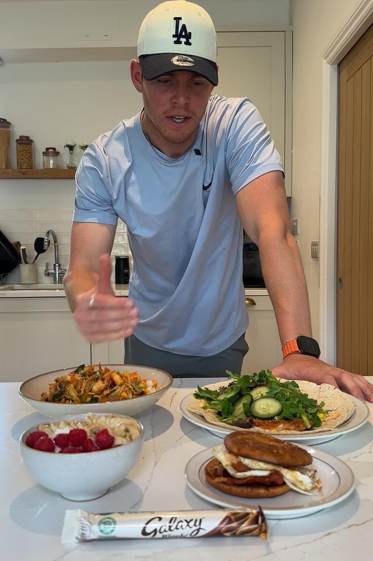 Paddy in his kitchen with protein-rich plates of food and a chocolate bar on the counter